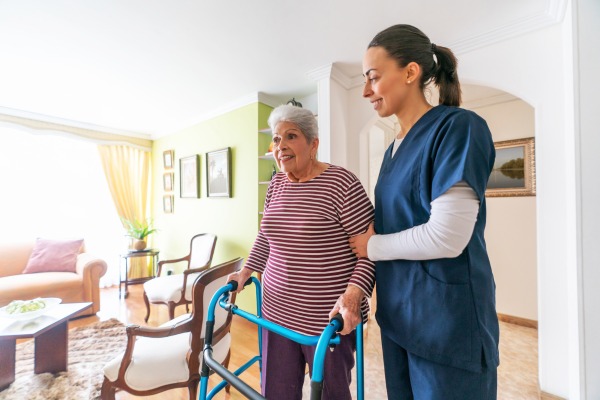 Female caregiver assisting senior with a walker moving to a assisted living facility.