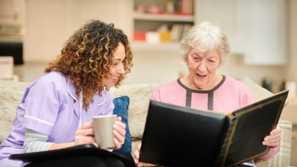 A senior resident of a memory care facility showing photo album to her caregiver.