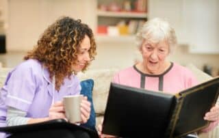 A senior resident of a memory care facility showing photo album to her caregiver.