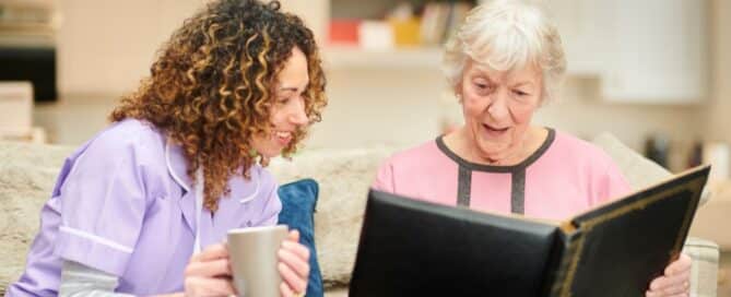 A senior resident of a memory care facility showing photo album to her caregiver.