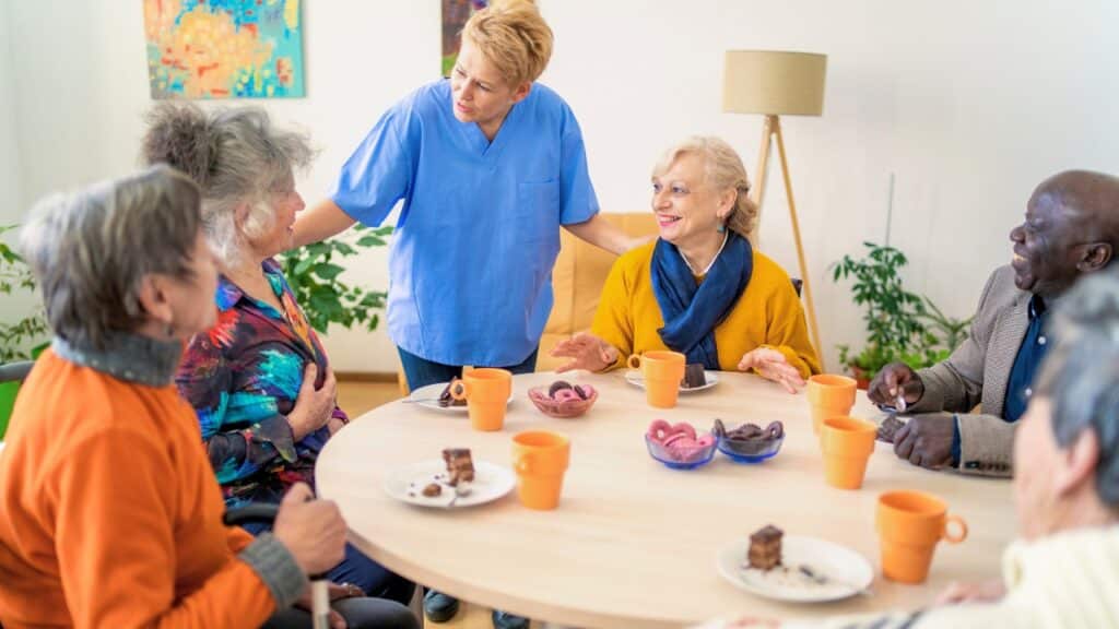 Caregiver and senior residents enjoying snack time in assisted living.