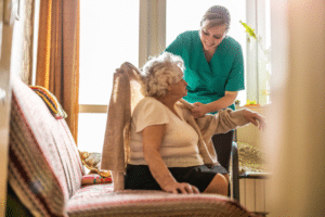 Female caregiver helping senior in dressing.