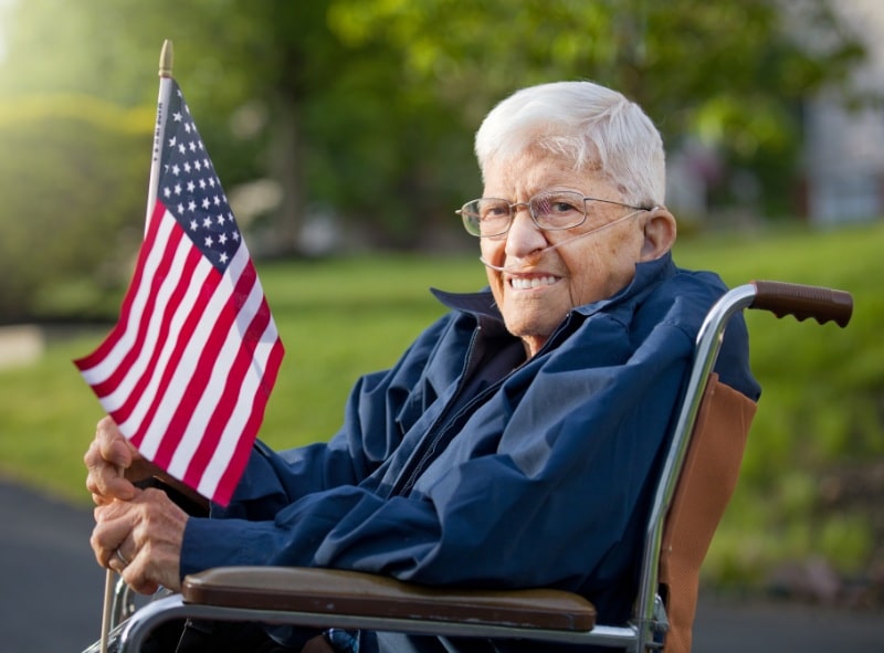 Elderly veteran in a wheelchair holding a US flag.