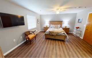 Heron East model bedroom with hardwood floors and a flat screen tv.