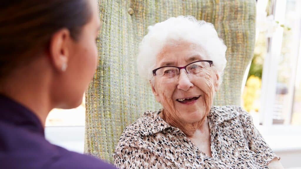 A female person talking to an elderly person in a chair. How to Overcome Guilt When Moving Parents to Senior Living