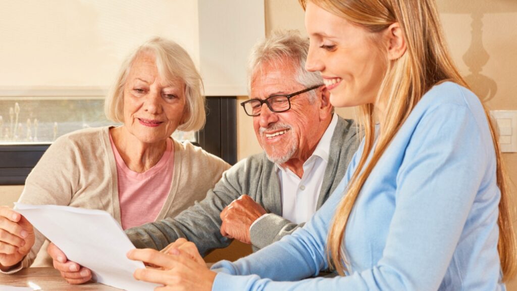 Two older people and a person sitting at a table with a piece of paper finding the right community for loved one.