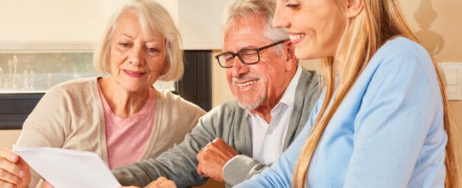 Two older people and a person sitting at a table with a piece of paper finding the right community for loved one.