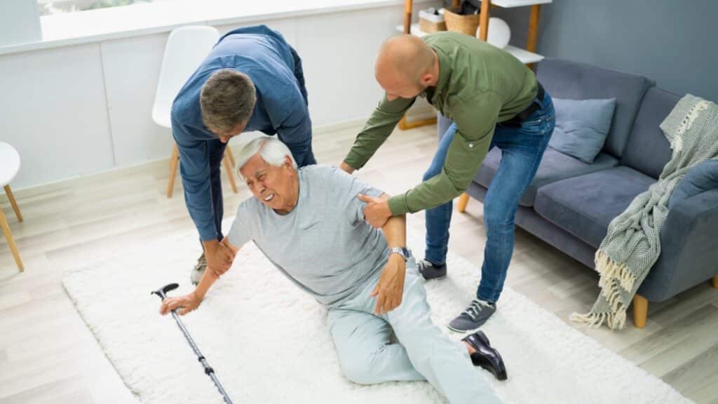 Two people helping a person who fell on the floor in a living room a factor to Find Senior Living Quickly During an Emergency.