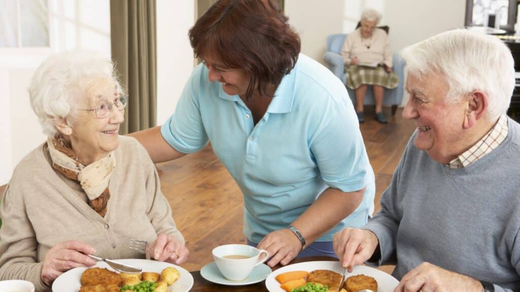 Senior couple eating assisted by caregiver when to move from independent to assisted living.