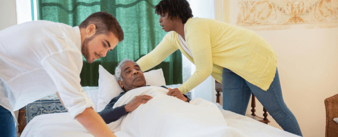 Two caretakers helping an elderly man to bed.