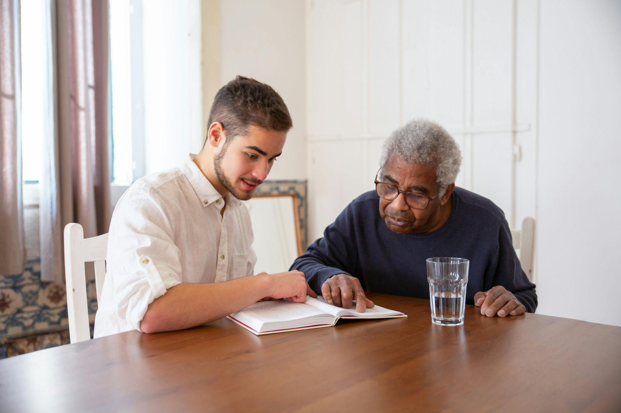 a caretaker and an old man reading together.
