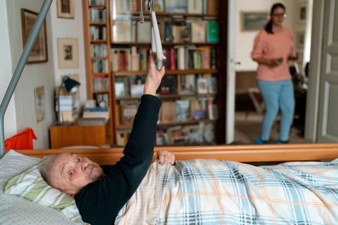 An elderly person lying in bed as their caretaker comes into the room