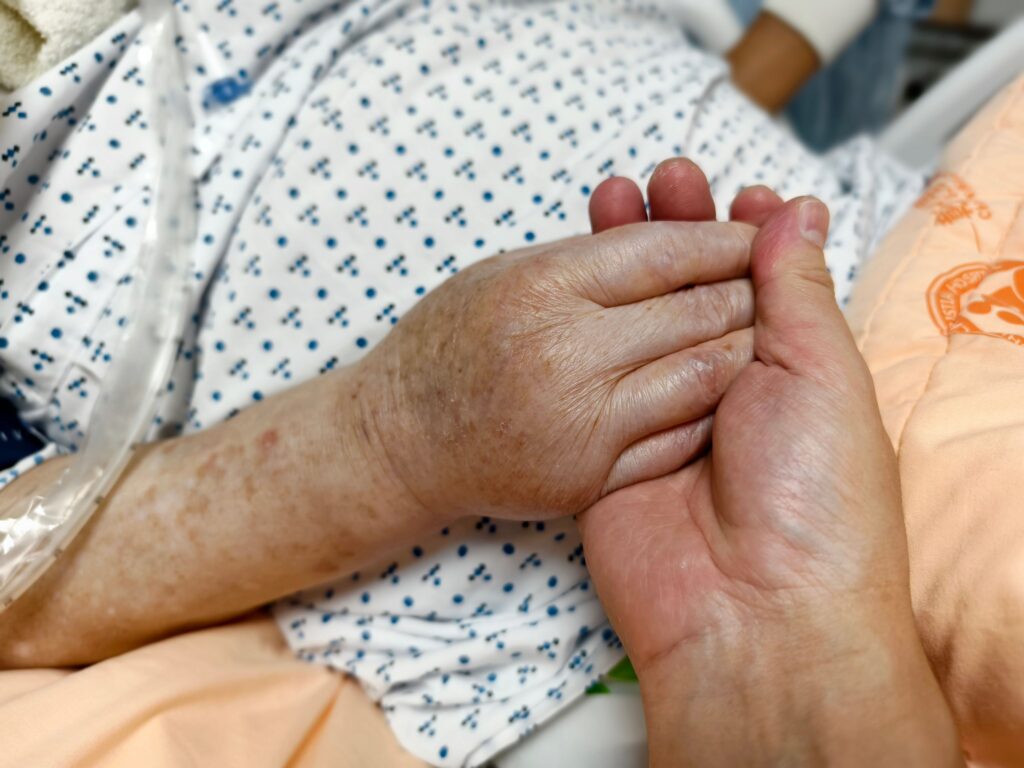 A senior person holding someone’s hands in the hospital