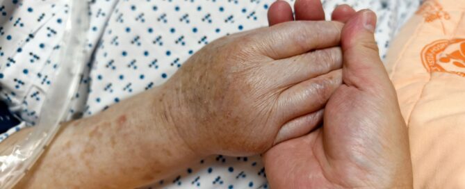 A senior person holding someone’s hands in the hospital