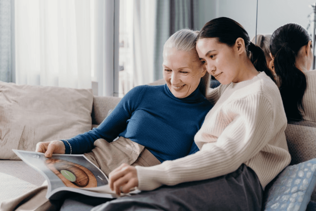 An elderly person and their child reading a magazine on the couch
