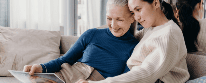 An elderly person and their child reading a magazine on the couch