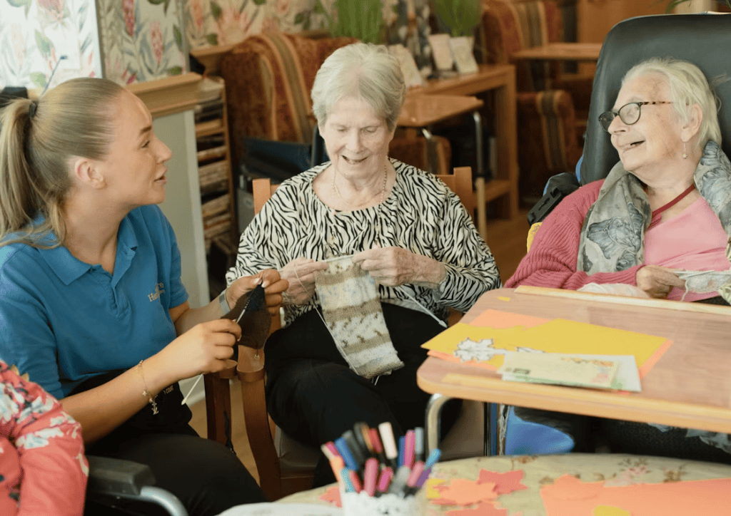A caregiver helping two elderly people with knitting 