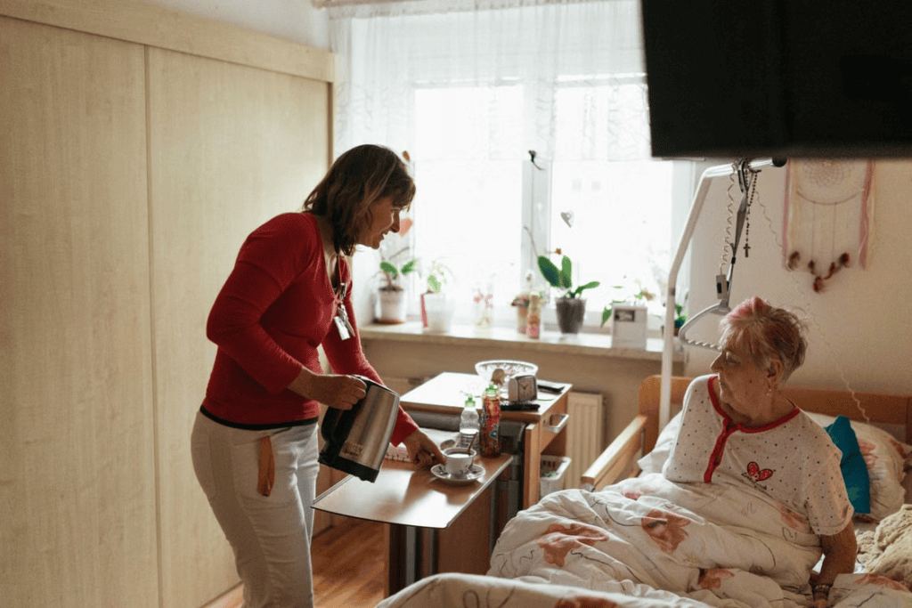 A caregiver serving a hot drink to an elderly person in bed