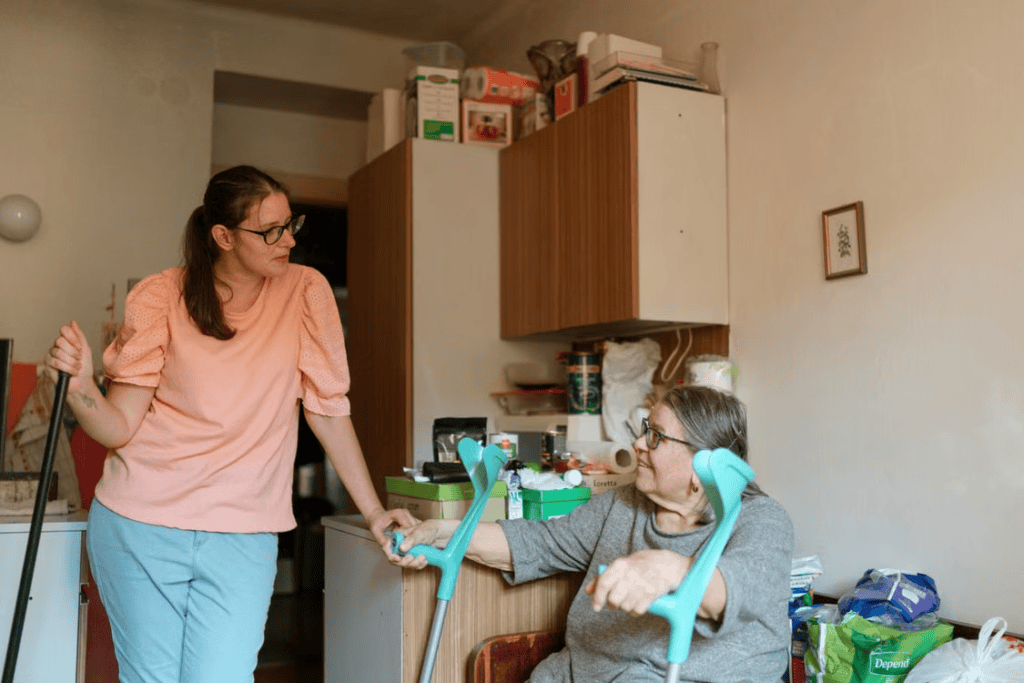 An elderly person holding crutches and talking to their caregiver