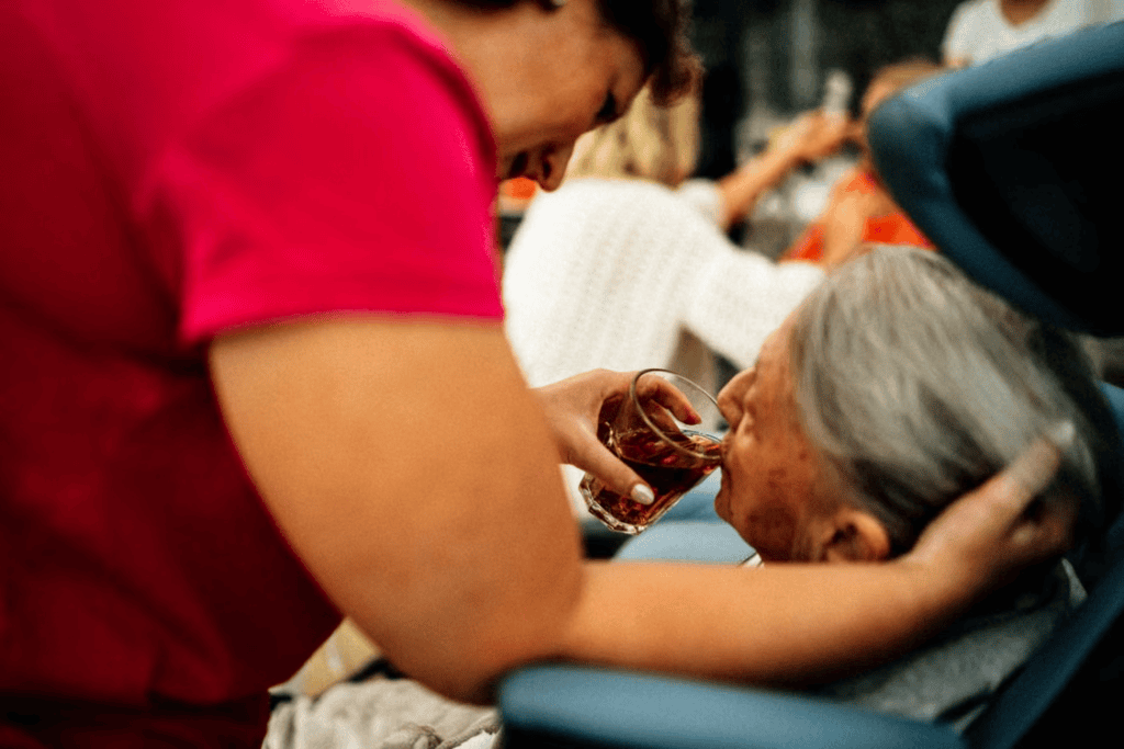 A caregiver helping an elderly person drink from a glass