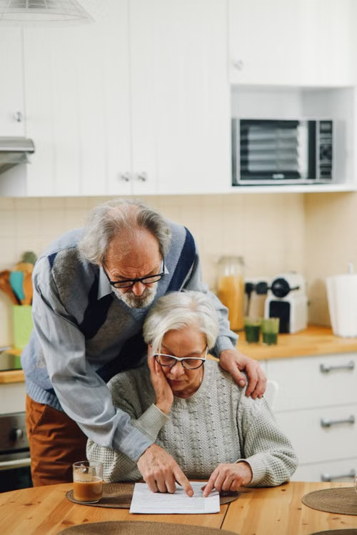 An elderly couple reviewing documents together at their kitchen table