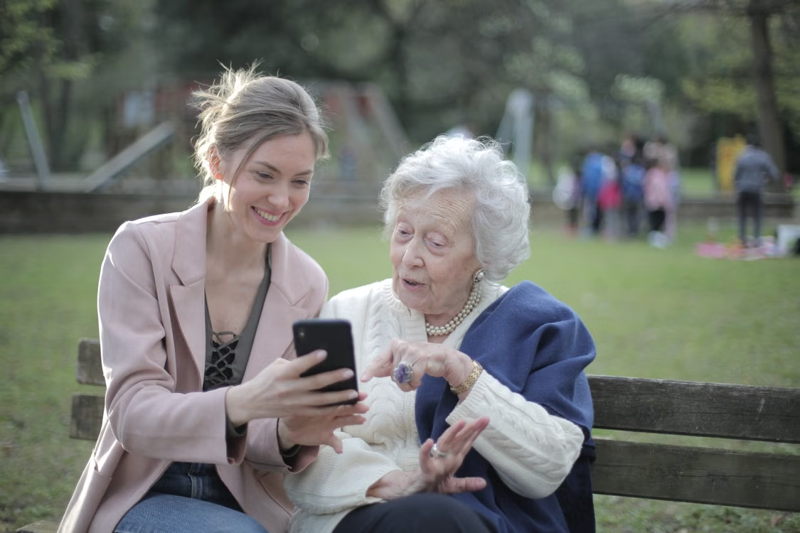 A senior mother and adult daughter smiling while looking at a phone together
